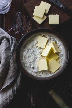 several pieces of cheese are in a bowl on a wooden table next to a knife