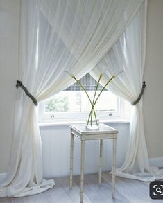 a vase with flowers sitting on a table in front of a white curtained window