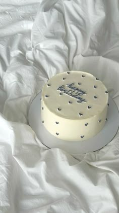 a white cake sitting on top of a bed covered in white sheets and blue hearts