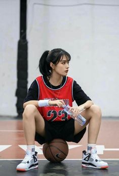 a young woman sitting on top of a basketball court holding a bat and wearing sneakers