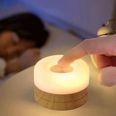 a person is touching the light on a small wooden table with a woman sleeping in the background