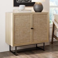 a sideboard with two doors and a vase on top in front of a window