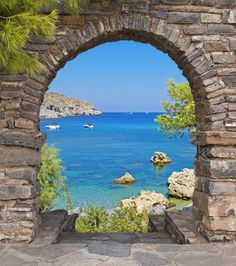 an arched stone wall with water and boats in the ocean behind it on a sunny day