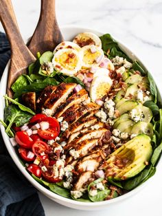 a salad with chicken, avocado and tomatoes in a white bowl on a marble table