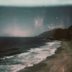 an old photo of the beach with waves coming in from the water and dark clouds