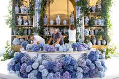 two men working on blue and white vases in front of shelves with greenery