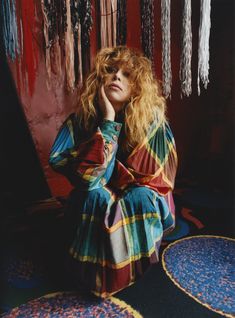 a woman sitting on the floor with her hands to her face, wearing a multicolored dress