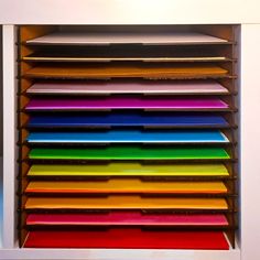 an assortment of colorful folders are stacked on top of each other in front of a white cabinet