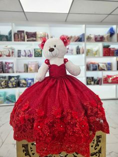 a white teddy bear wearing a red dress sitting on top of a wooden box in a store