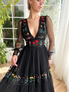 Elevate your wardrobe with our enchanting dress, meticulously crafted from a soft, dotted black tulle fabric that beautifully drapes the body. Adorned with delicate embroidered whimsical flowers, this dress features a flattering V-neckline and a sculpted bustier top that hugs close, accentuating your silhouette. The ti Fitted V-neck Tulle Dress, A-line Tulle Dress With Floral Embroidery, Elegant Long Sleeve Embroidered Dress For Garden Party, Elegant Long Sleeve Embroidered Garden Party Dress, Long Sleeve Tulle Dress With Floral Embroidery, Long Sleeve Floral Embroidered Tulle Dress, Sheer V-neck Dresses With Fitted Bodice, Elegant Floral Embroidered Dress With Sweetheart Neckline, Floral Embellished V-neck Evening Dress