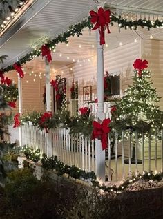 a house decorated for christmas with red bows and lights on the front porch, covered in greenery