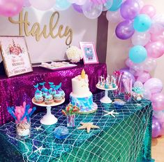 a table topped with cakes and cupcakes under balloons