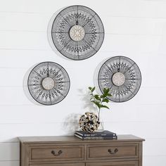 two metal wall hangings on the side of a dresser in a room with white walls