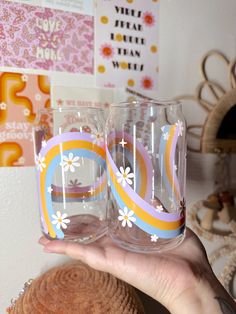 two glasses with flowers painted on them are being held by a woman's hand