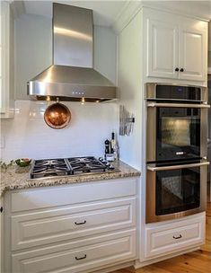 a kitchen with white cabinets and stainless steel stove top oven, range hood, and wooden flooring