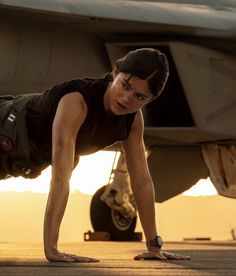 a woman is doing push ups in front of an airplane with her hands on the ground