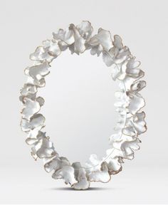 a circular mirror with white flowers on it's sides and an oval frame in the middle