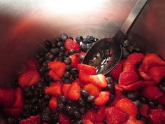 berries and blueberries are mixed together in a metal bowl with a ladle to stir them