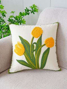 a white pillow with yellow flowers on it sitting on a chair next to a potted plant