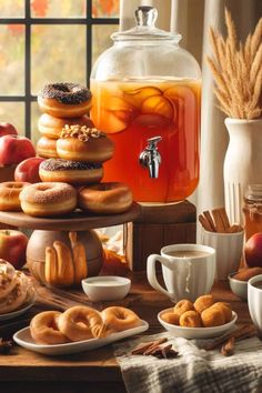 a table topped with lots of donuts next to a pitcher of tea and cups