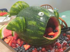 a watermelon shaped like a fish with its mouth open surrounded by berries and strawberries