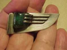 a person holding a small metal fork in their left hand with a green stone on it