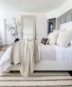 a white bed with pillows and blankets on top of it in a bedroom next to a mirror