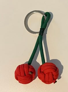 two red balls are tied to a green rope on a white surface with a metal hook