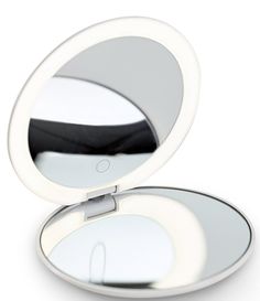 a white compact mirror with its reflection in it's lid and light reflecting on the surface