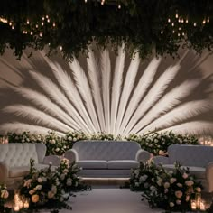 an elegant wedding setup with white flowers, candles and peacock feathers on the wall behind it