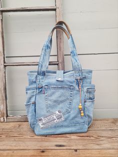 An everyday shoulder bag made from a pair of vintage lightblue Levis jeans with details preserved.  Jeans lining as handle with leather details Handles are long enough for you to care it on your shoulder.  7 outer pockets and 4 within.  Close bag with snap button  red/white inner lining with cute zipper pocket.  Sturdy bottom (something leftover from a construction site, my shop is all about no waste and I reuse things I get my hands on that fits my style 🙂) last pic are for size and style refe Denim Blue Upcycled Travel Bag, Denim Travel Bag With Upcycled Material, Recycled Denim Hobo Bag For Everyday Use, Upcycled Denim Travel Bag, Upcycled Denim Hobo Shoulder Bag, Upcycled Shoulder Bag In Recycled Denim, Upcycled Recycled Denim Shoulder Bag, Upcycled Medium Wash Denim Shoulder Bag For Everyday Use, Upcycled Medium Wash Recycled Denim Shoulder Bag