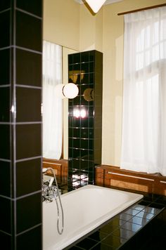 a bath tub sitting next to a window in a bathroom with black tile on the walls