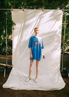 a woman standing in front of a white backdrop wearing a blue shirt dress and white tennis shoes