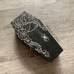 a black and white box with spider webs on the lid sitting on a wooden table