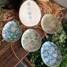 four blue and white plates sitting on top of a wooden table next to green plants