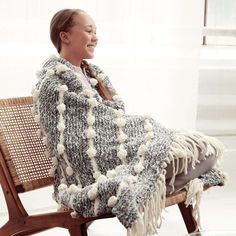 a woman is sitting on a chair wrapped in a blanket and smiling at the camera