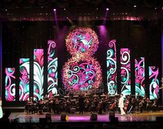 the stage is lit up with purple and blue lights, while an orchestra plays on it