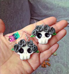 a pair of skull earrings with roses in the shape of skulls on their backs, are being held by a woman's hand