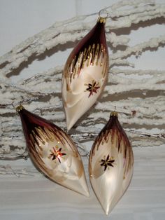 three glass christmas ornaments hanging on a white wall with snow flakes in the background