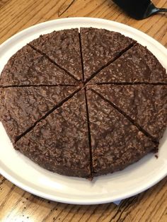 a chocolate cake on a white plate sitting on a wooden table with utensils