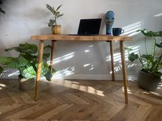 a wooden table topped with a laptop computer next to potted plants and greenery