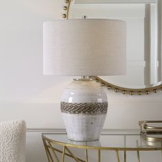 a white vase sitting on top of a glass table next to a mirror and lamp