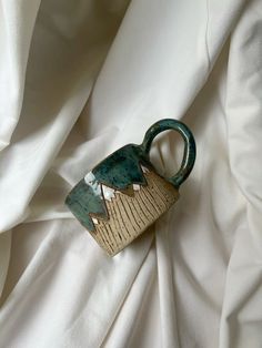 a ceramic teapot sitting on top of a white cloth covered tablecloth with an abstract design