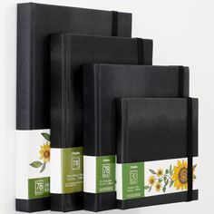 three black notebooks are lined up against a white wall with sunflowers on them