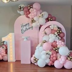 pink and white balloons are on display in front of a number one balloon arch for a 1st birthday party