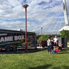 people standing in front of a game box truck on the grass near a street light