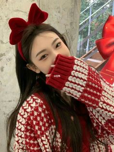 a woman with long hair wearing red and white knitted sweater holding up her hand to her face