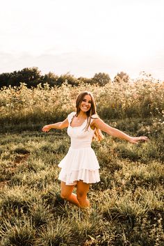 a woman in a white dress is standing in the grass with her arms spread out