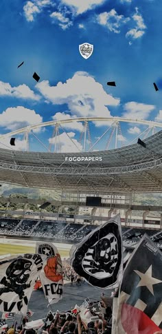 fans are holding flags in front of an empty stadium with blue sky and white clouds