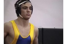 a young man wearing a yellow and blue wrestling singlet is looking at the camera